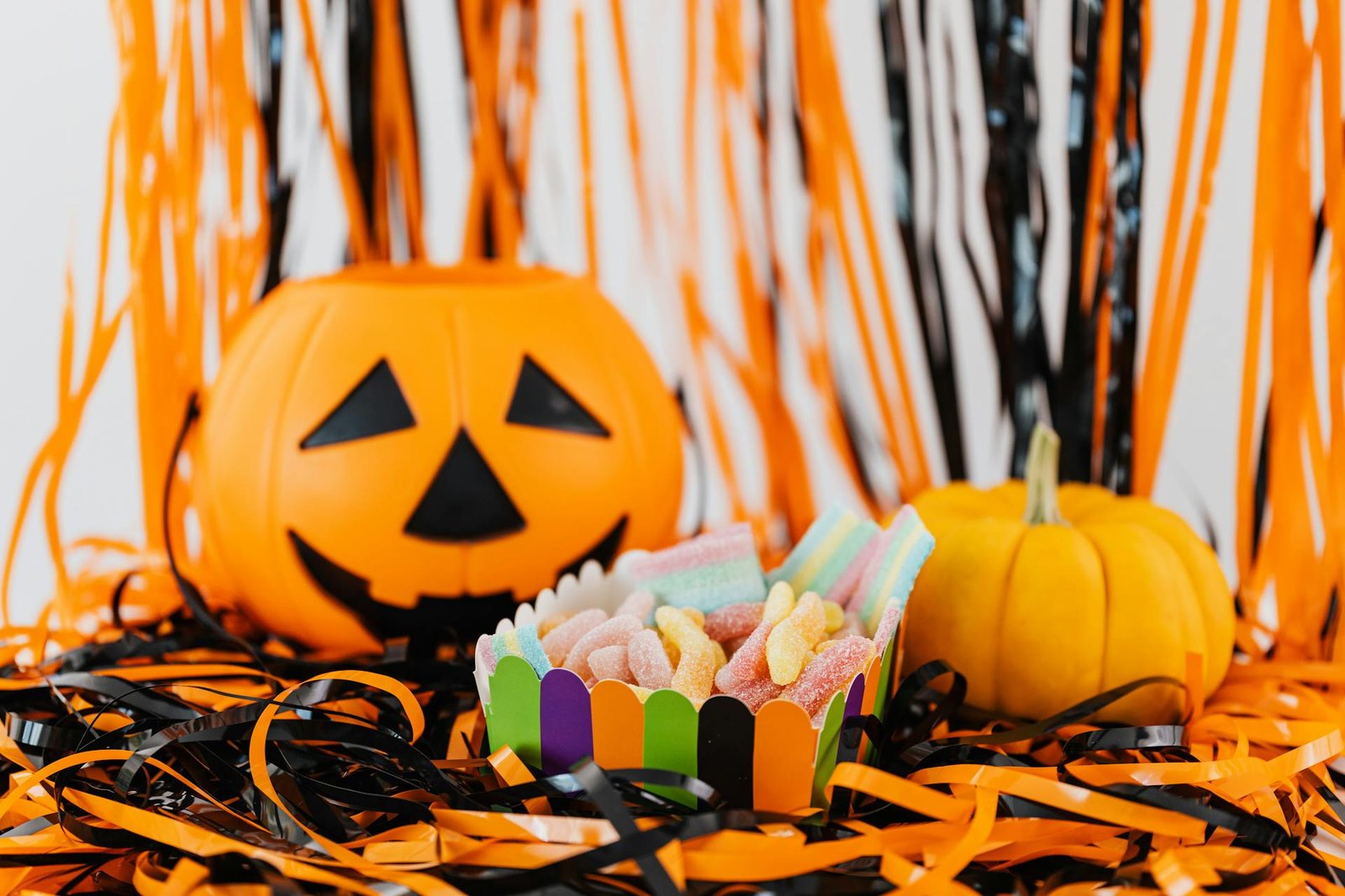 Colorful Halloween candies in a festive paper cup surrounded by pumpkins and orange and black streamers