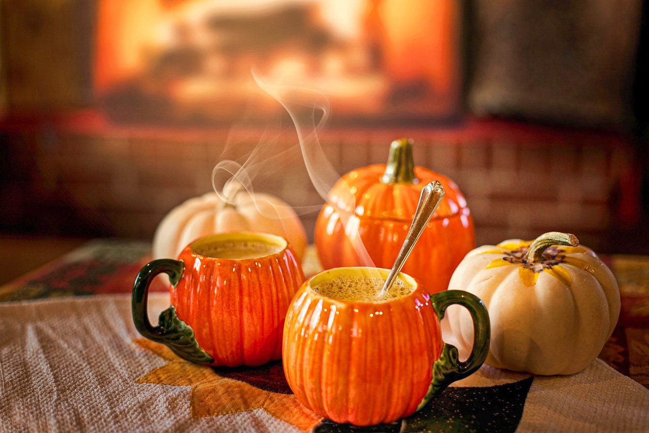 Pumpkin spice lattes served in pumpkin shaped mugs, surrounded by decorative pumpkins, set on a cozy autumn table