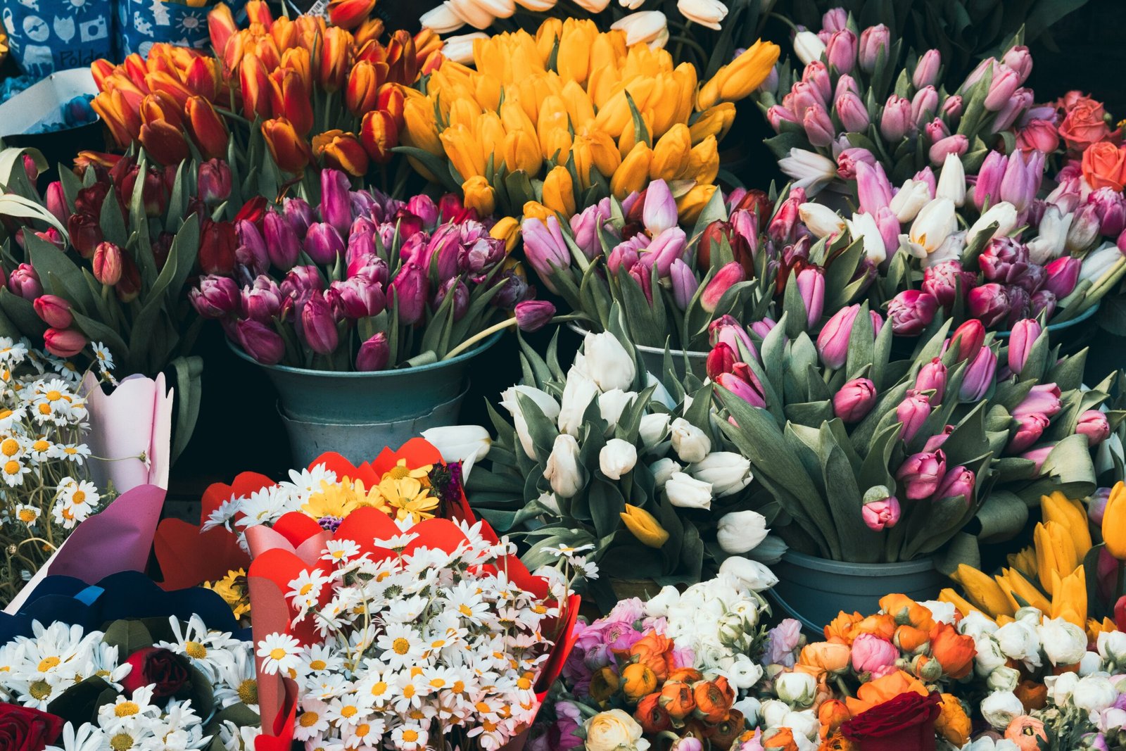 Colorful bouquets of fresh tulips, daisies, and other seasonal flowers displayed at an outdoor flower market.