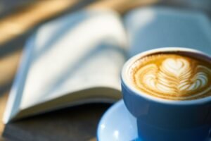 Cup of latte with heart shaped latte art beside an open book in warm mornings, creating a cozy reading atmosphere.