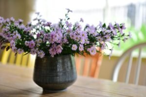 Vase of delicate purple wildflowers on a wooden table, bringing a soft and cozy touch to a bright, sunlit room