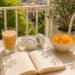 Soft life summer scene with a journal, iced coffee, headphones, fresh flowers, and seasonal fruit on a sunny balcony table.