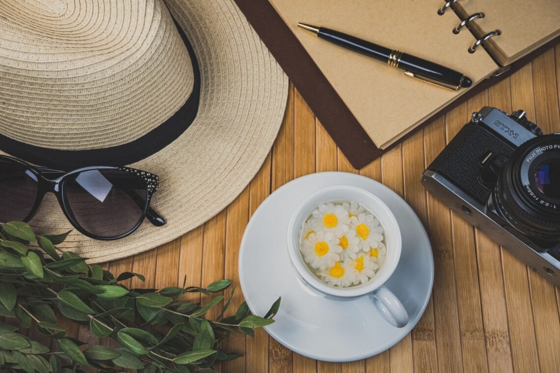 Summer flatlay with a camera, sunglasses, journal, flowers, and iced drink on a wooden table