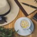 Summer flatlay with a camera, sunglasses, journal, flowers, and iced drink on a wooden table