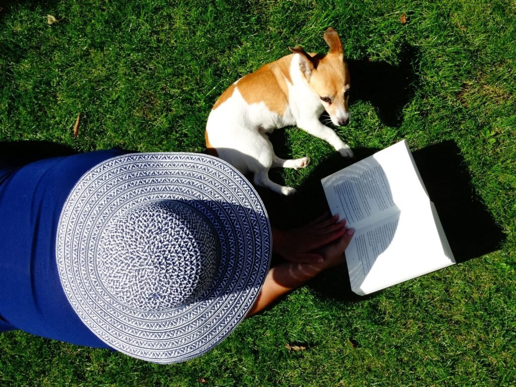 Person reading a book outdoors on the grass with a dog