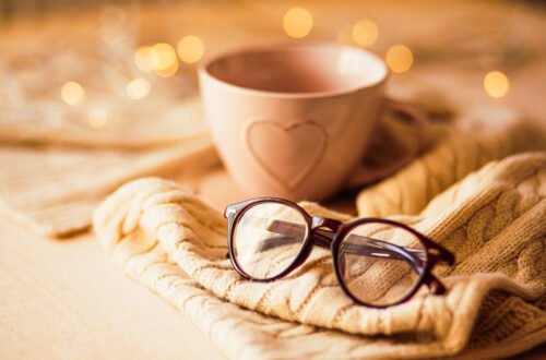 Cozy September journaling scene with a warm mug, open journal, knitted sweater, and glasses on a wooden table, illuminated by soft golden lights.