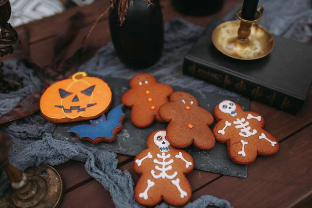 Halloween themed cookies shaped like pumpkins, bats, ghosts, and skeletons arranged on a dark slate board .